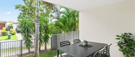 Un balcón con una mesa y sillas, una planta en maceta y vistas de un jardín con palmeras.