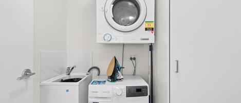 A compact laundry area with a front-loading washer and dryer, a small sink, and a wall-mounted ironing board.
