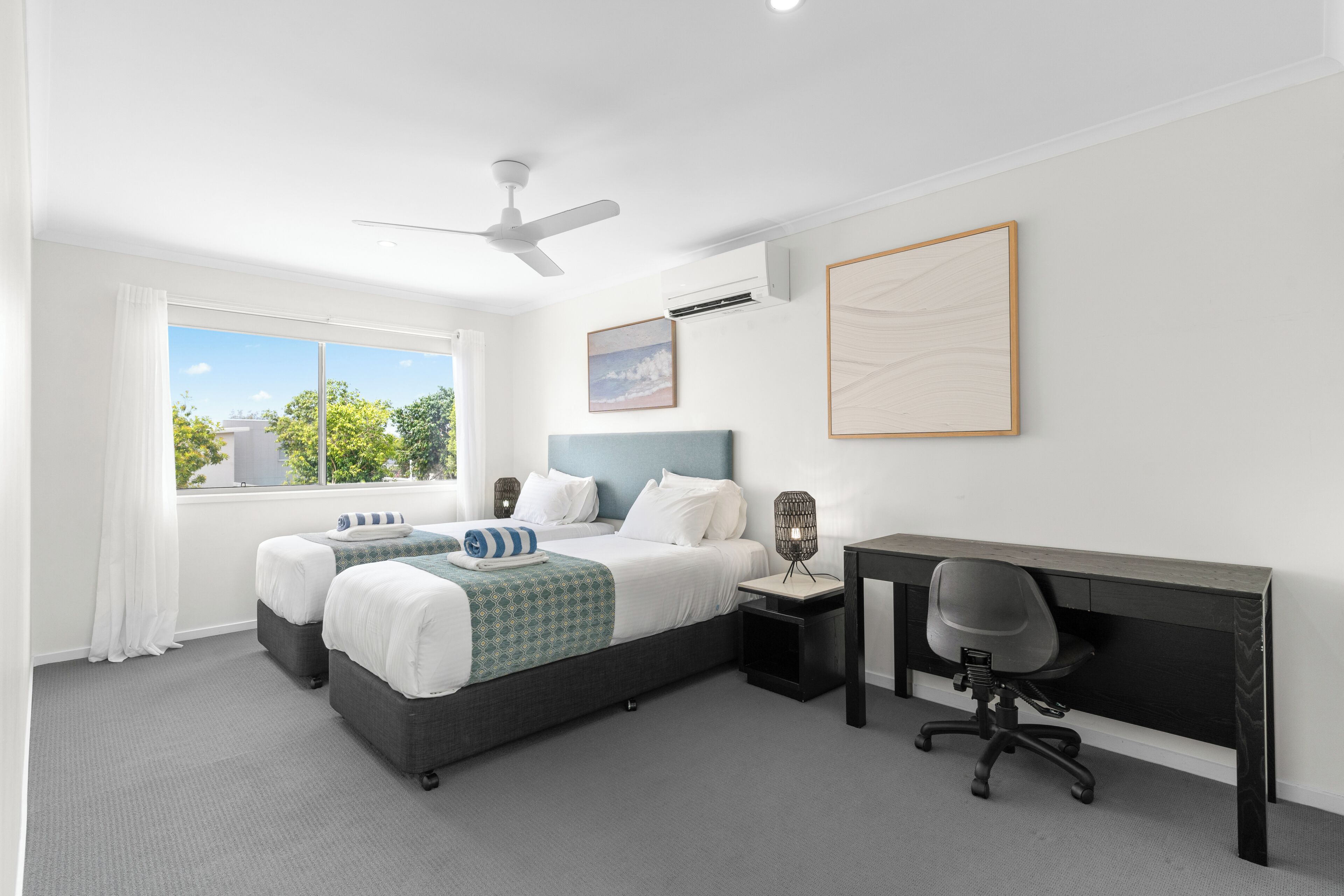 A modern hotel room with a bed, desk, chair, and large window.