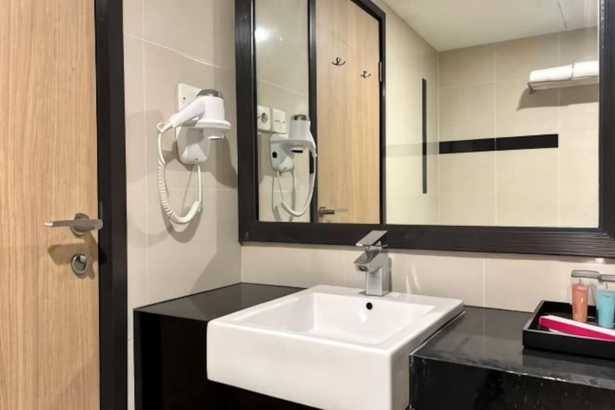 Een badkamer met een wit wastafel, een spiegel en een haardroger bevestigd aan de muur.