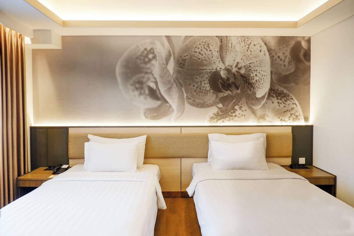 A hotel room with two beds, a large orchid artwork on the wall, and a wooden headboard.