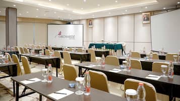 A conference room at Orchardz Hotel with multiple tables, chairs, and a projection screen.