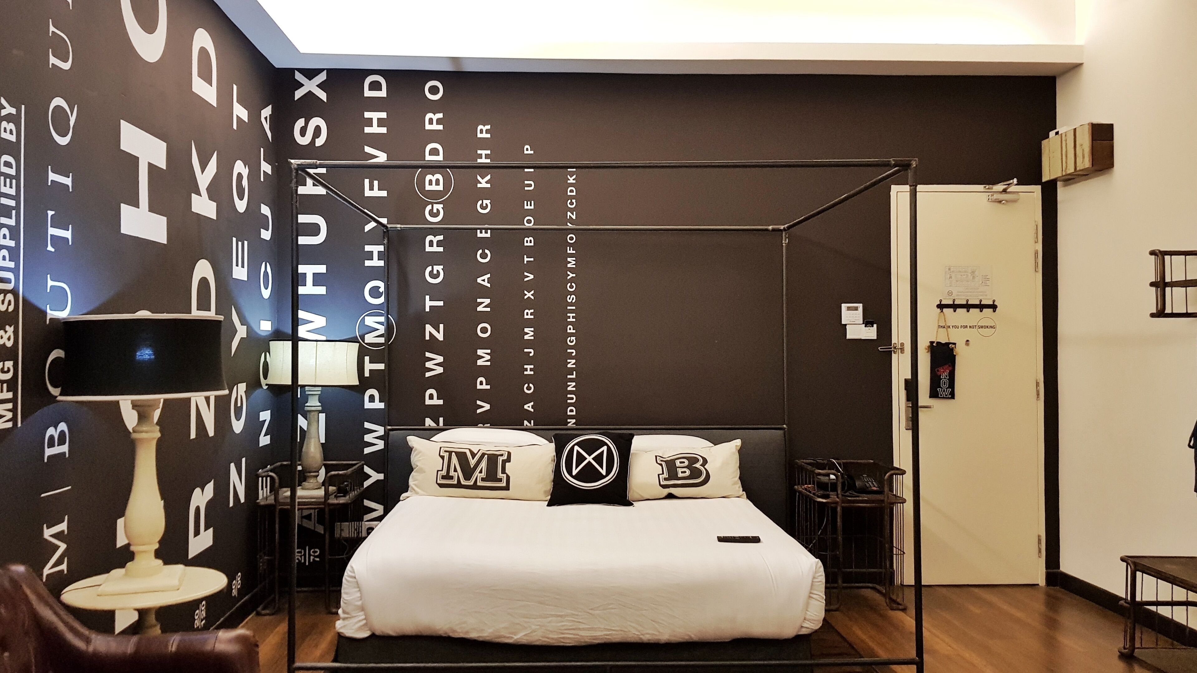 Un dormitorio con cama con dosel, una mesita de noche con lámpara y una pared decorada con letras del alfabeto.