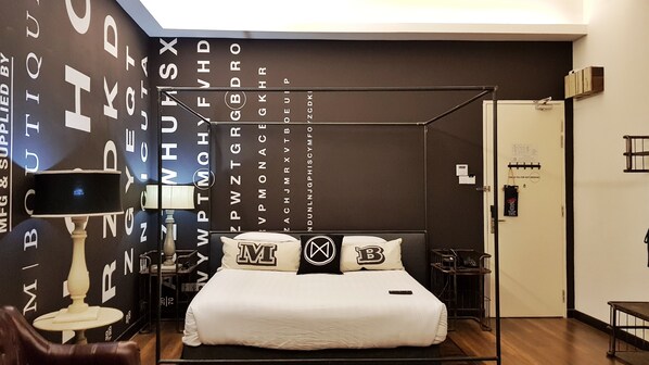 A bedroom with a four-poster bed, a nightstand with a lamp, and a wall with alphabet letters. - M Boutique Station 18 (Ipoh)