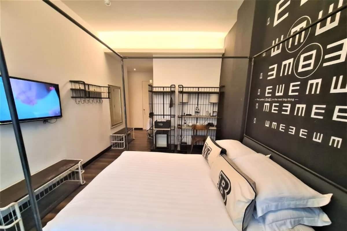 A modern hotel room with a large bed, a TV mounted on the wall, and a blackboard with text.