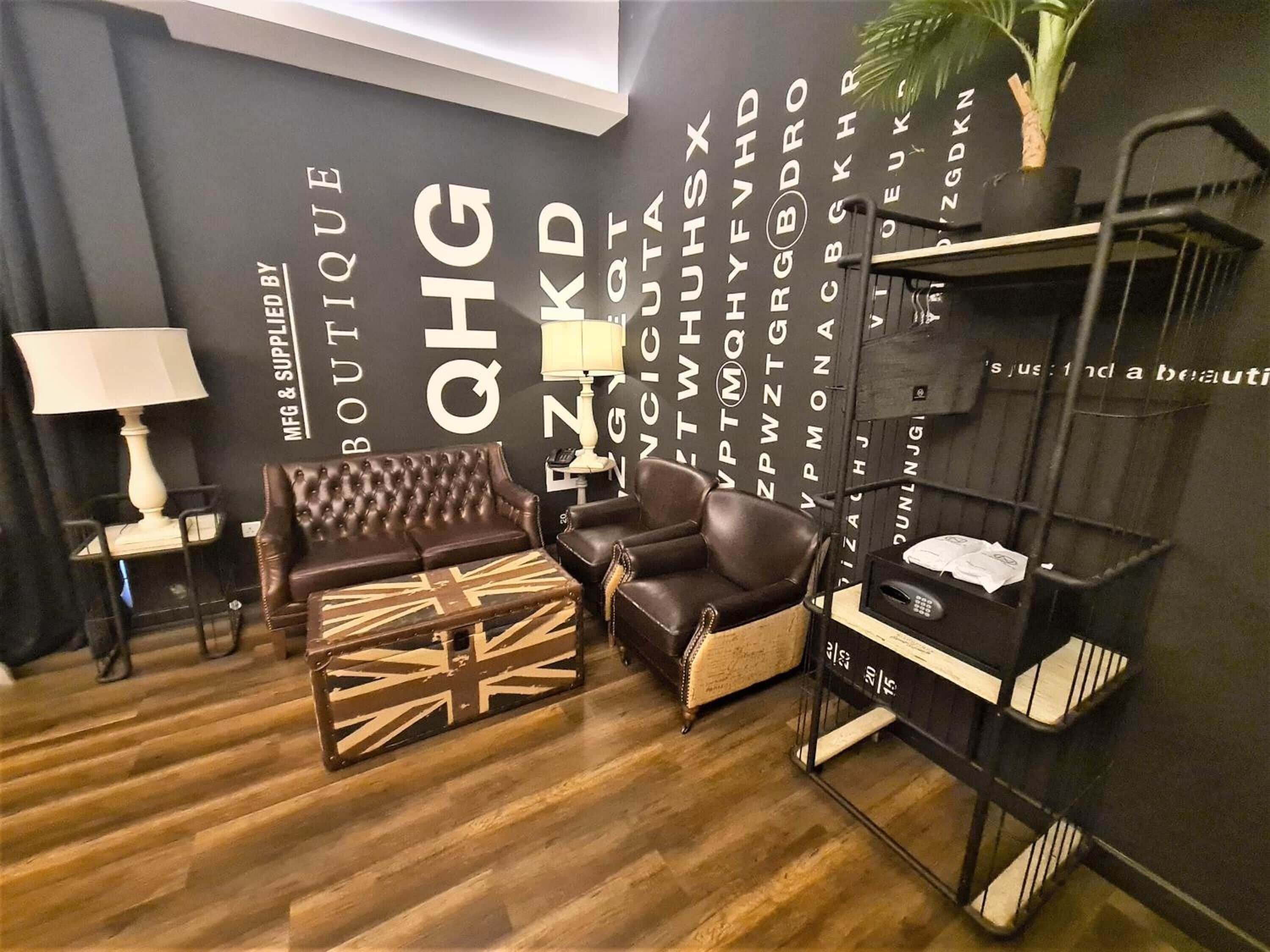 A modern living room with a dark wall, a brown leather sofa, a matching armchair, and a small table with a lamp.