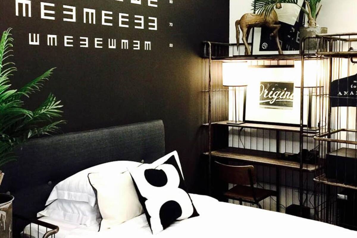 A bedroom with a bed, a wall with text, a desk, a chair, and a potted plant.