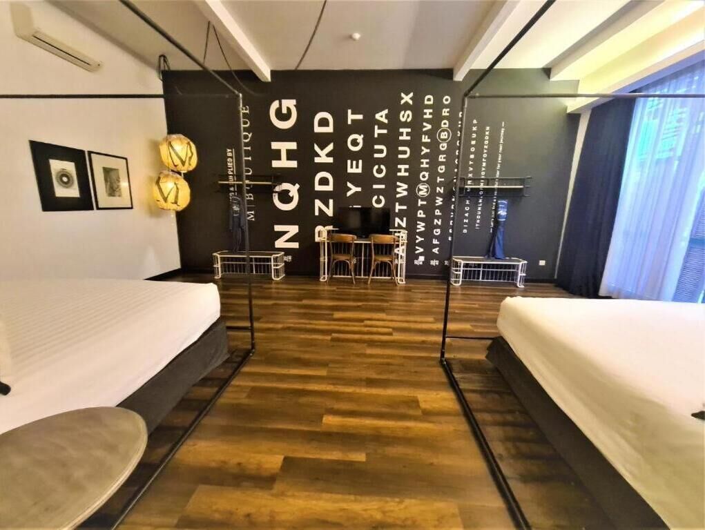 Una habitación de hotel moderna con dos camas, piso de madera, pared de acento negra con texto blanco y un ventanal grande.