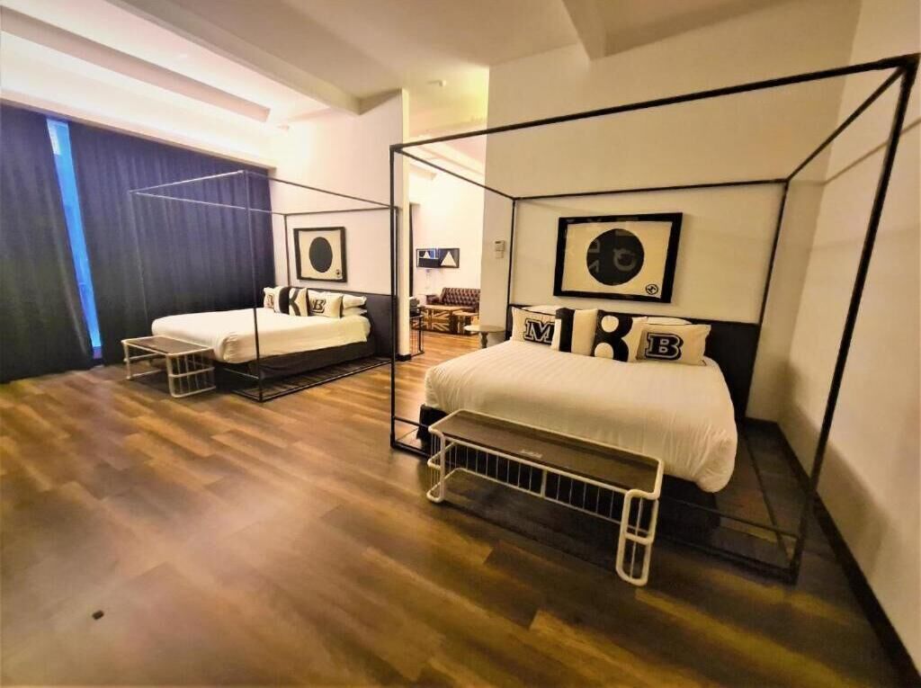 A modern hotel room with a four-poster bed, a small bedside table, and a large window with curtains.