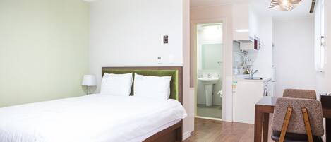 Habitación de hotel con cama, escritorio y silla. Se ve un baño por una puerta abierta.