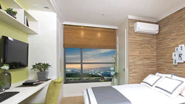 Un dormitorio moderno con una cama, un escritorio y un amplio ventanal con vistas a la ciudad.