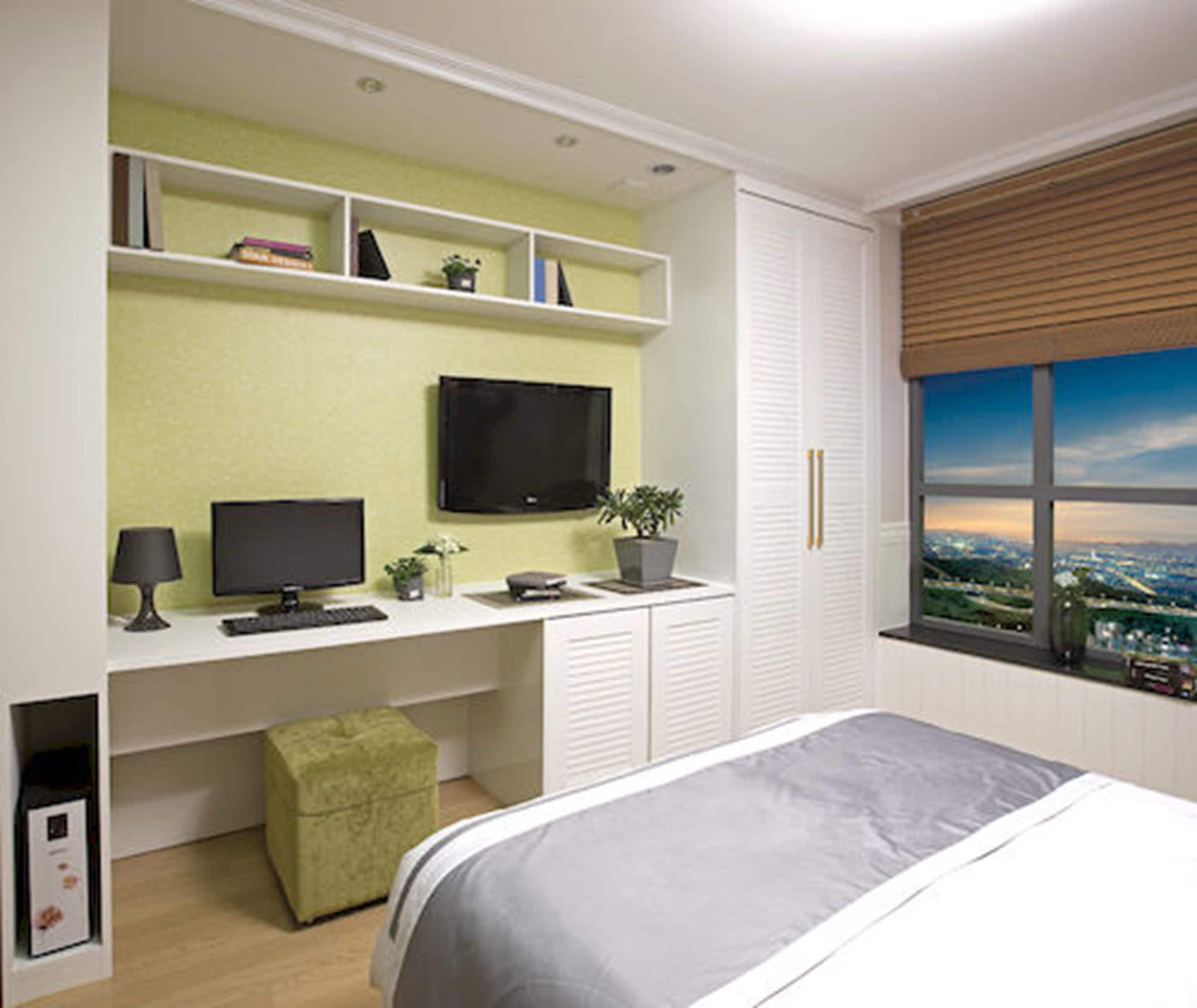 Une chambre à coucher avec un lit, un bureau avec un ordinateur, une télévision et une fenêtre donnant sur la ville.