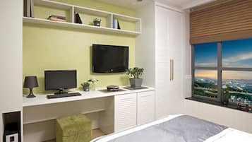 Un dormitorio con una cama, un escritorio con computadora, un televisor y una ventana con vista a la ciudad.