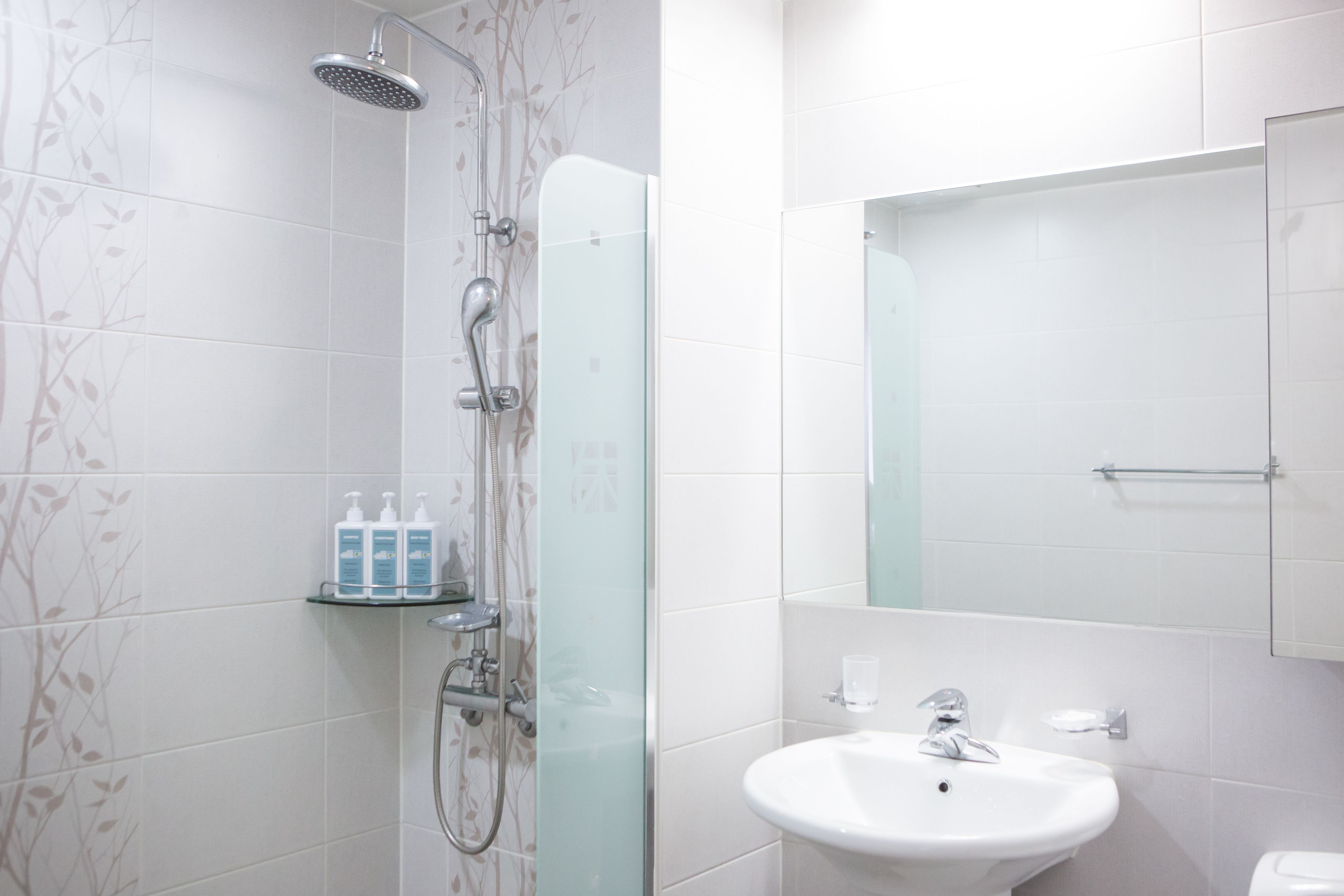Un baño moderno con cabina de ducha de vidrio, un lavamanos blanco y un espejo sobre él.