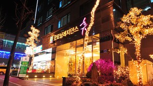Un hotel con fachada de vidrio, señalización iluminada y árboles decorados con luces.