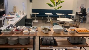 Un área de comedor moderna con mesas de buffet, que incluye diversos alimentos y utensilios.