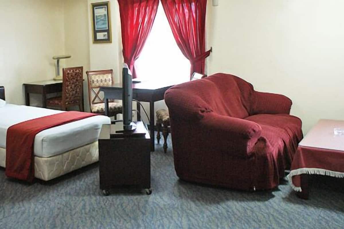 Quarto de hotel com duas camas, um sofá vermelho, uma escrivaninha com luminária e uma cadeira.