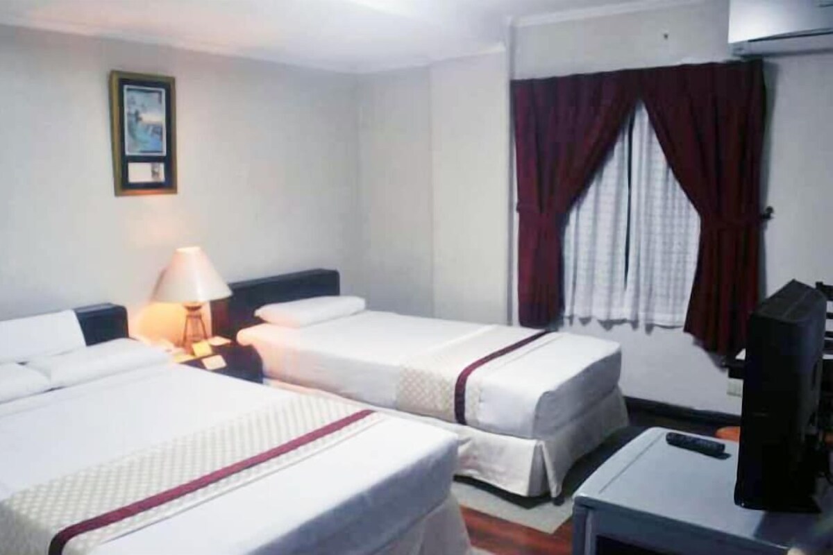 Habitación de hotel con dos camas, un escritorio con computadora, una lámpara y una ventana con cortinas.