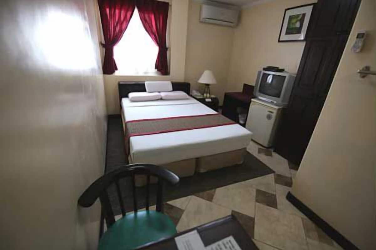 Quarto de hotel com cama, escrivaninha, cadeira, televisão e janela com cortinas.