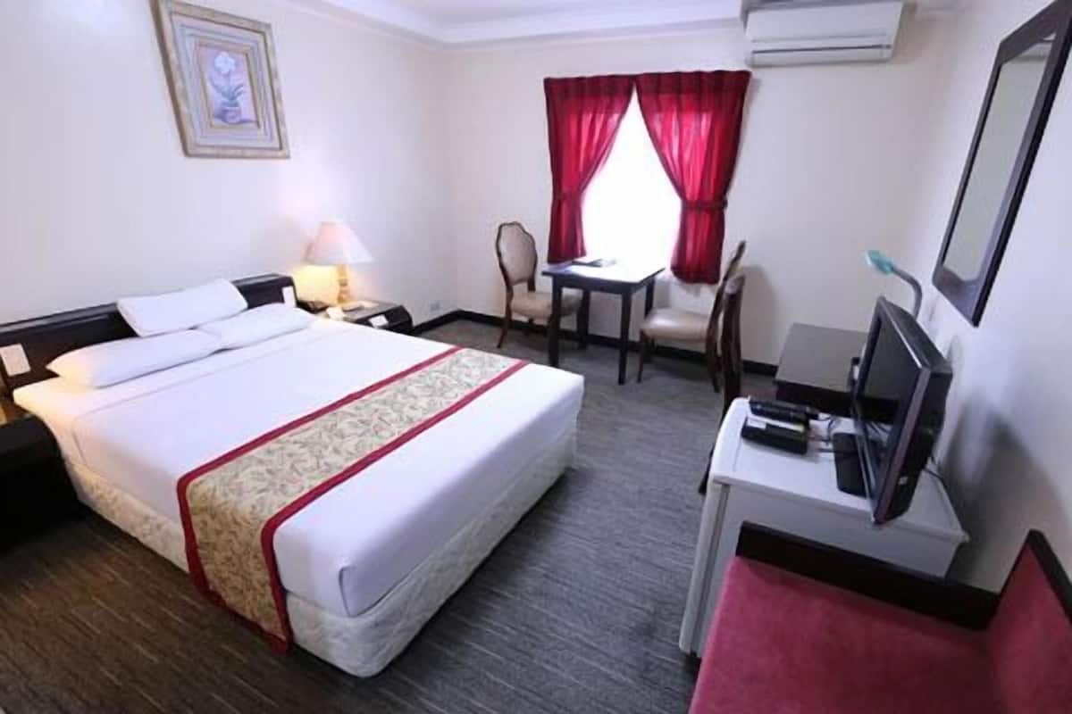 Quarto de hotel com cama, secretária com computador, cadeira, mesa e janela com cortinas vermelhas.