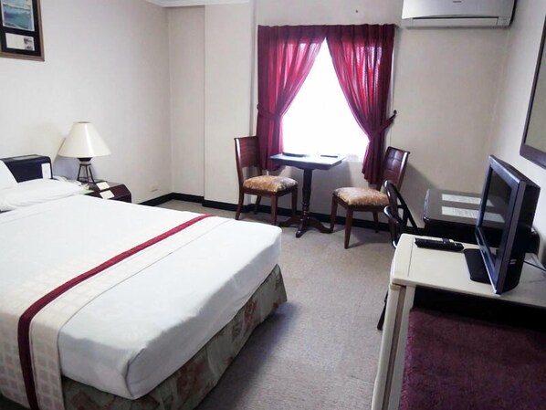 A hotel room with a bed, a desk, two chairs, a TV, and a lamp.