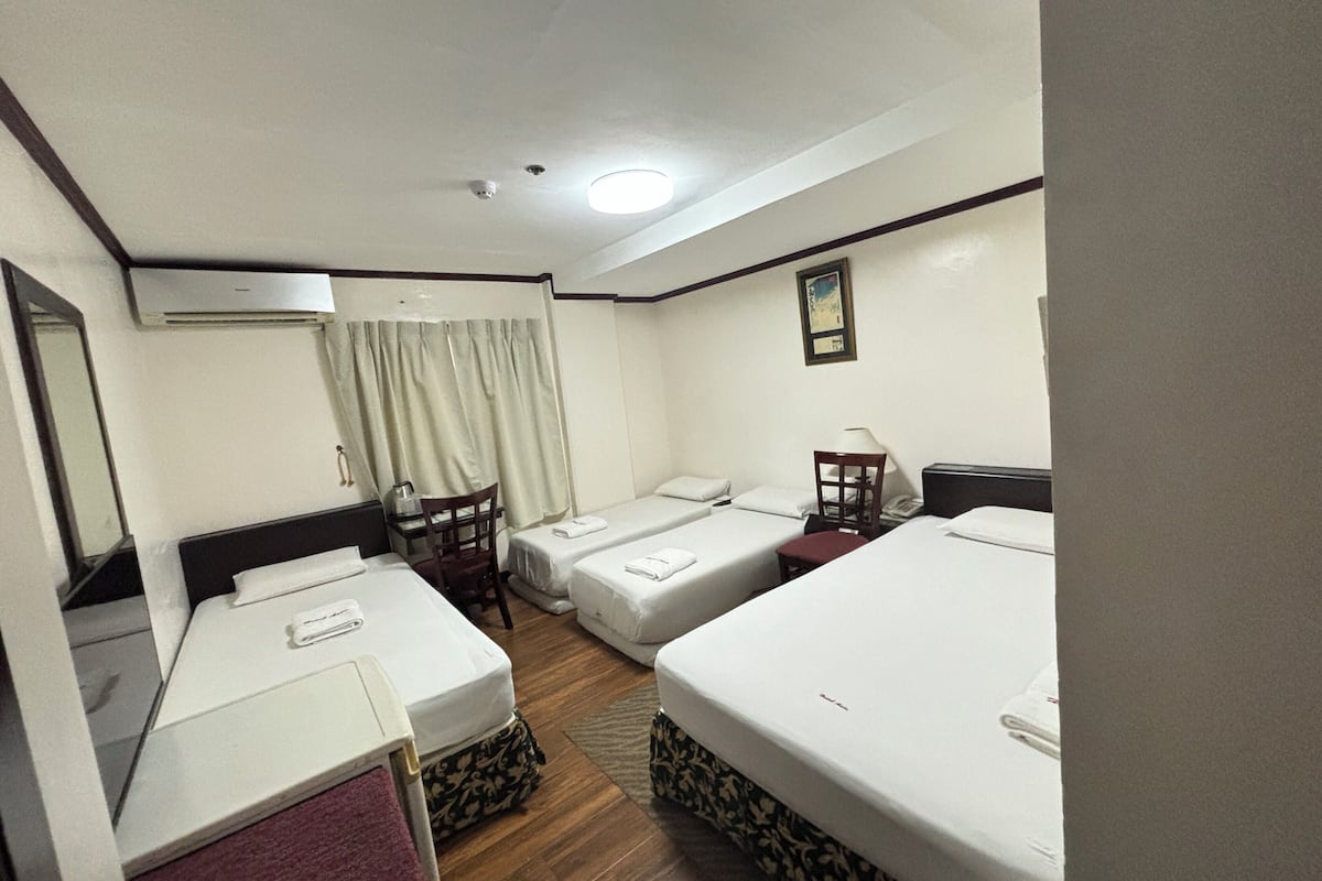 Quarto de hotel com duas camas de solteiro, uma mesa com cadeira, uma mesinha com abajur e um espelho na parede.