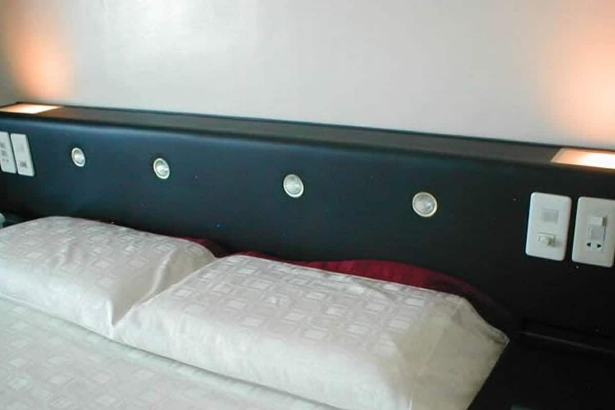Cama com cabeceira que inclui vários interruptores de luz e uma tomada.