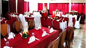 Ein Festsaal mit runden Tischen, die mit roten Tischdecken bedeckt sind, weißen Stühlen und roten Vorhängen.
