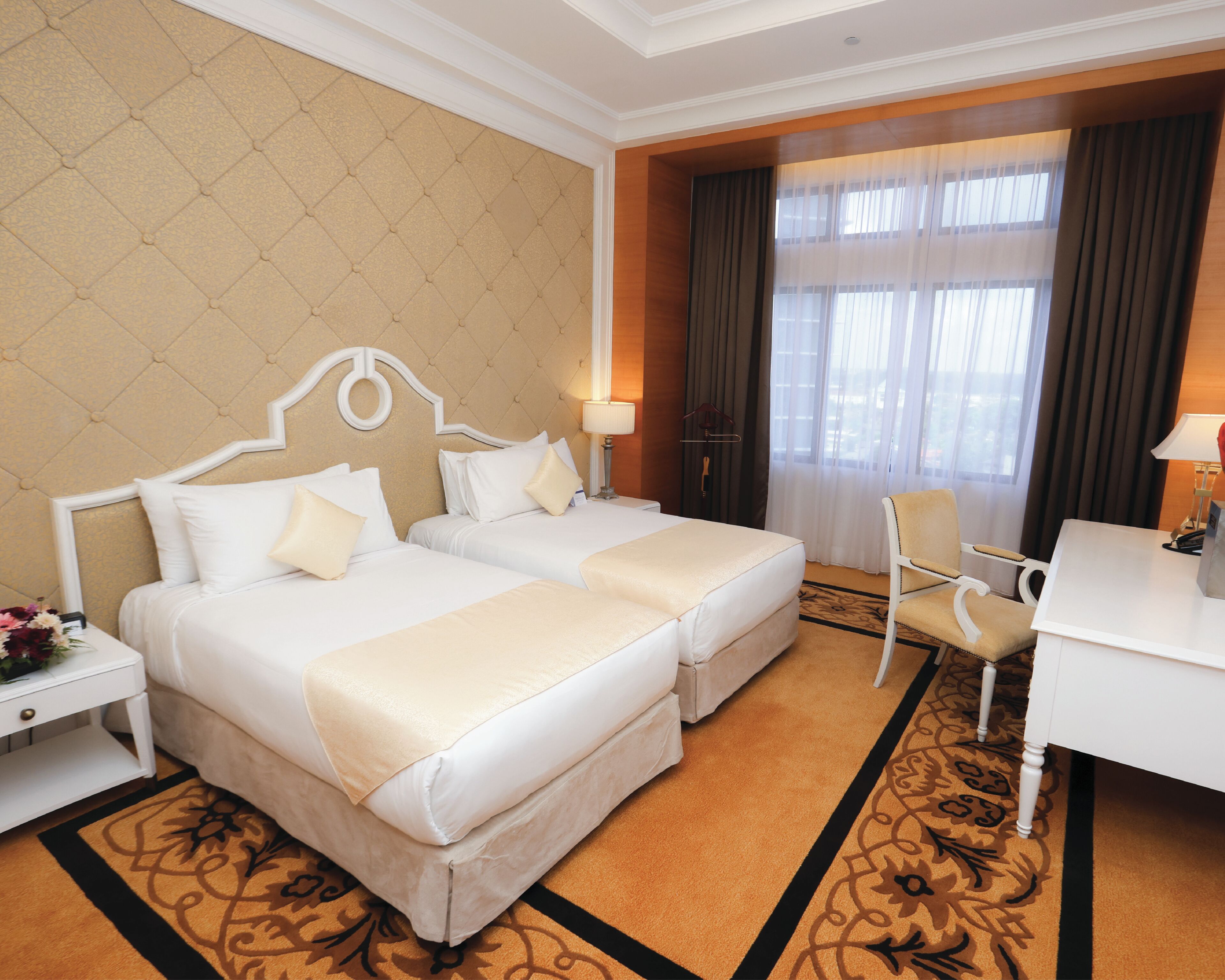 A hotel room with two beds, a desk, a chair, and a large window with curtains.