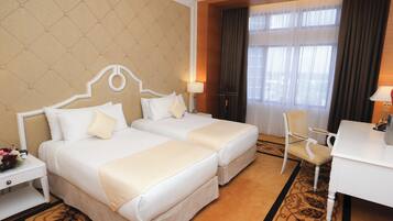 A hotel room with two beds, a desk, a chair, and a large window with curtains.