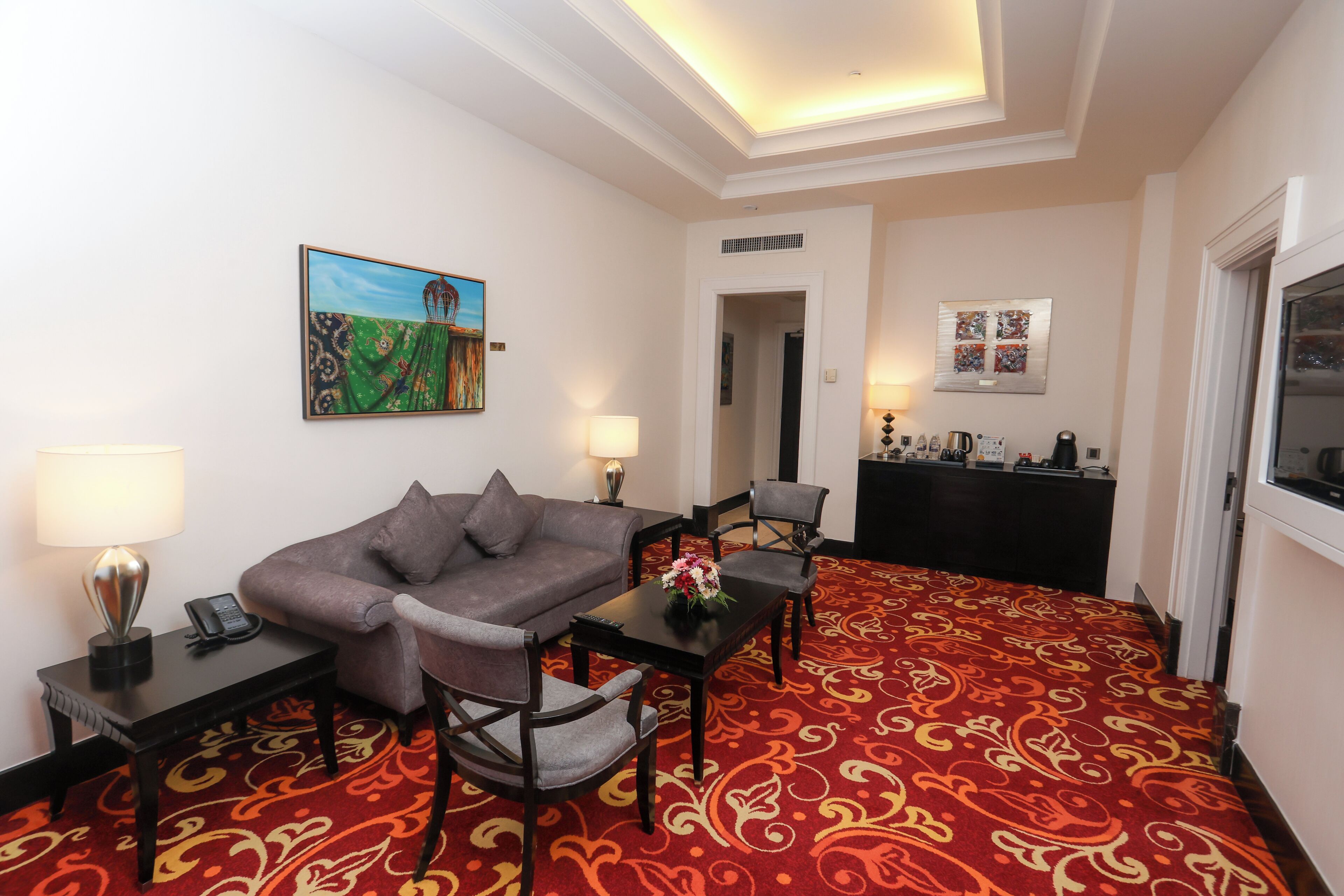 A hotel room with a sofa, chairs, a coffee station, and artwork on the walls.
