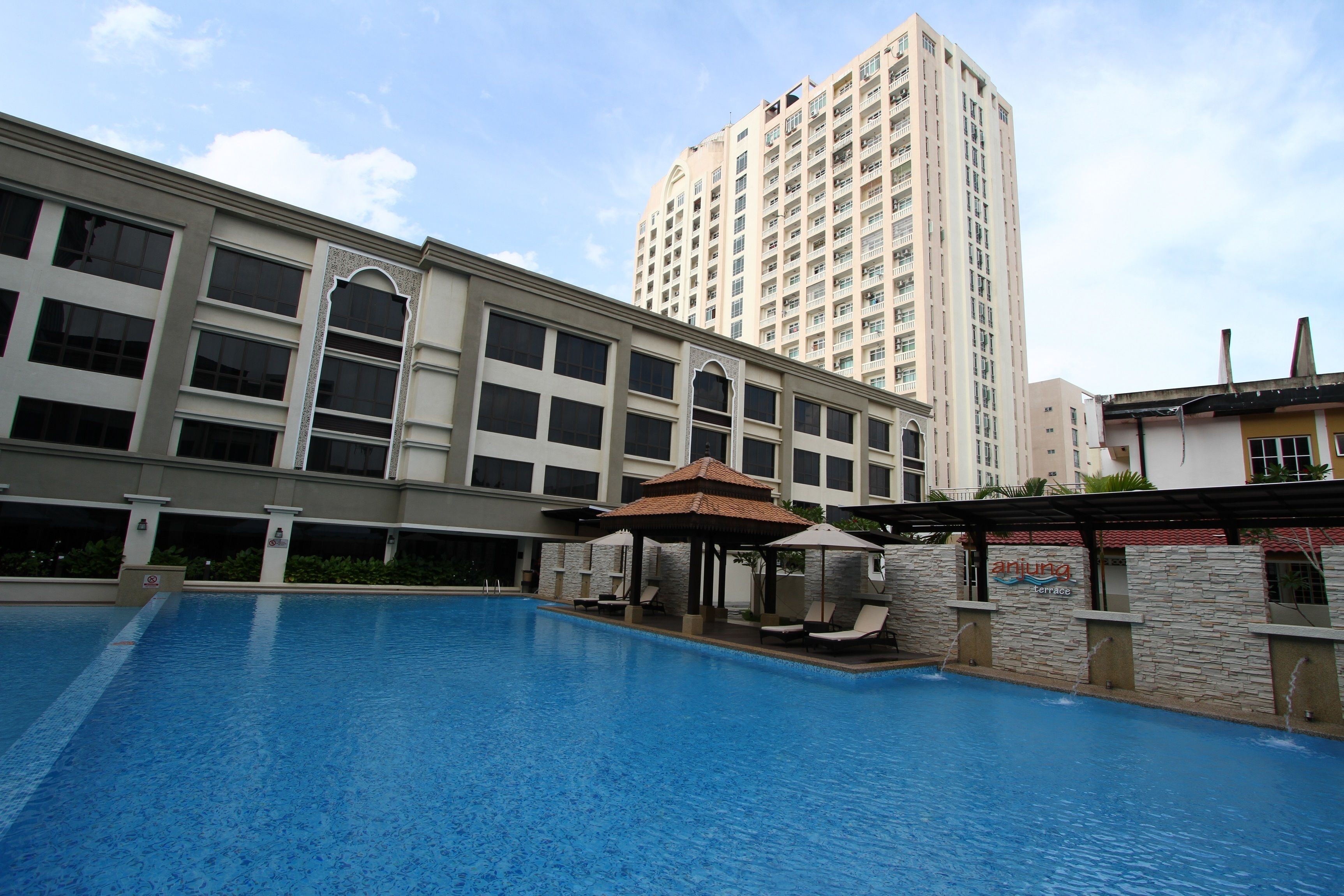 A swimming pool with lounge chairs and a gazebo, surrounded by a building with multiple windows and a tall residential building in the background.