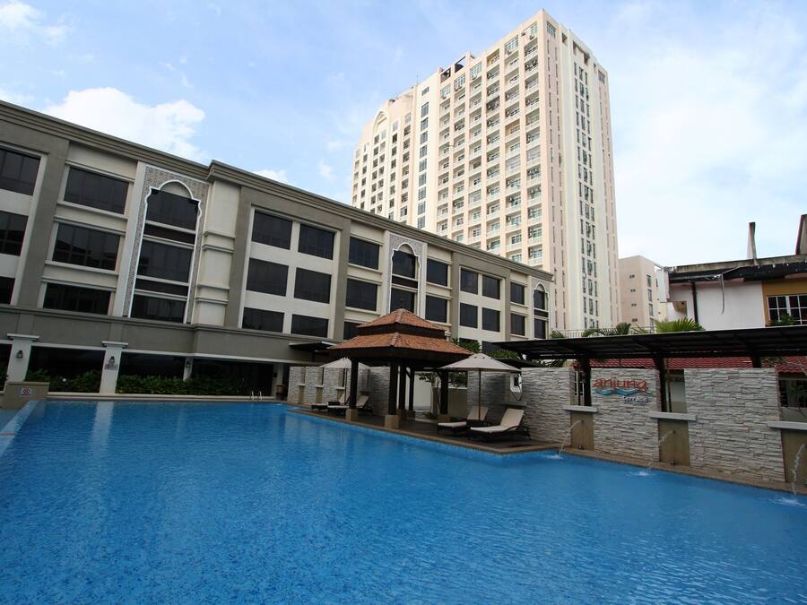 Piscina com espreguiçadeiras e um gazebo, cercada por um edifício com várias janelas e um prédio residencial alto ao fundo.