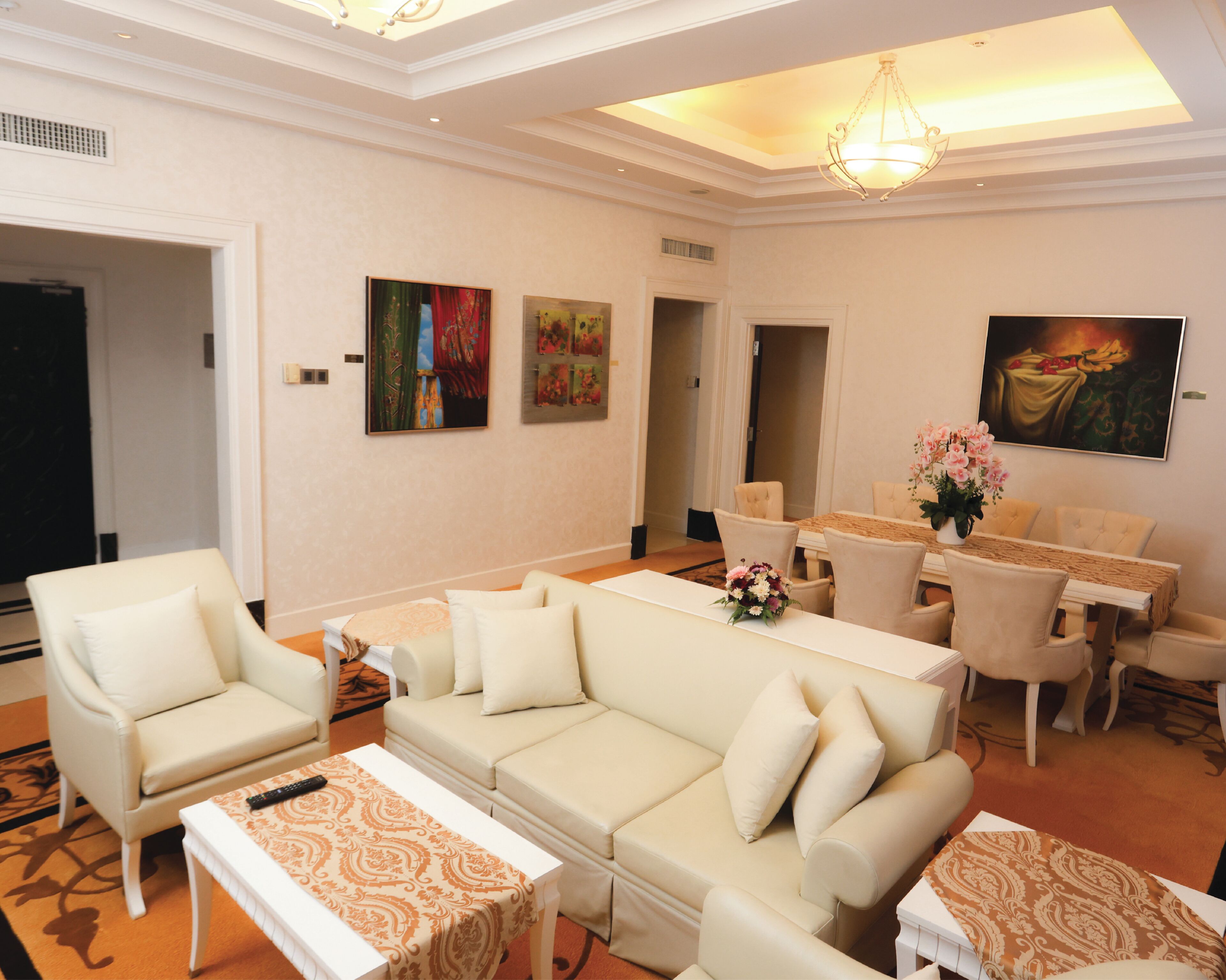 Een hotelkamer met een bank, fauteuil, eettafel en kunstwerken aan de wanden.