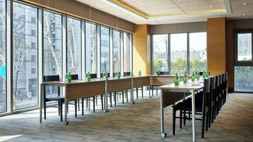 Un salón de conferencias con ventanas amplias, una mesa larga con sillas y botellas verdes sobre la mesa.