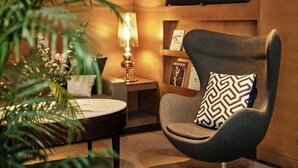 A modern living room with a round coffee table, a grey armchair with a patterned pillow, a floor lamp, and a bookshelf with framed pictures. - Mayplace Seoul (Seoul)