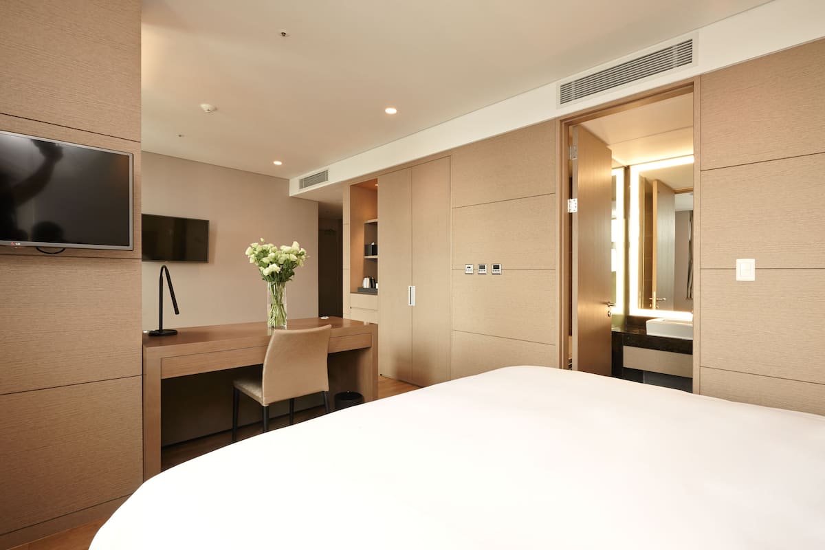 A modern hotel room with a large bed, a desk with a chair, a flat-screen TV, a vase with flowers, and a large mirror.