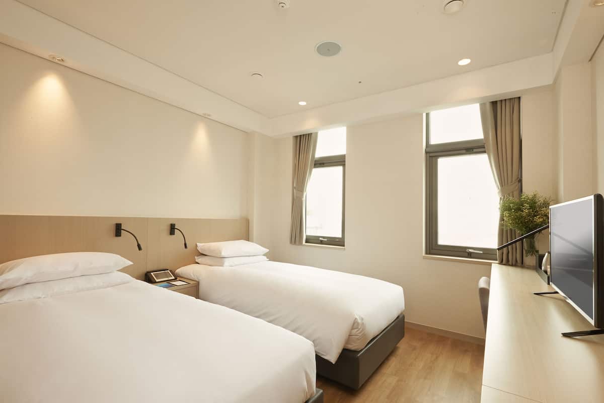 A hotel room with two beds, a desk with a TV, and a window with curtains.