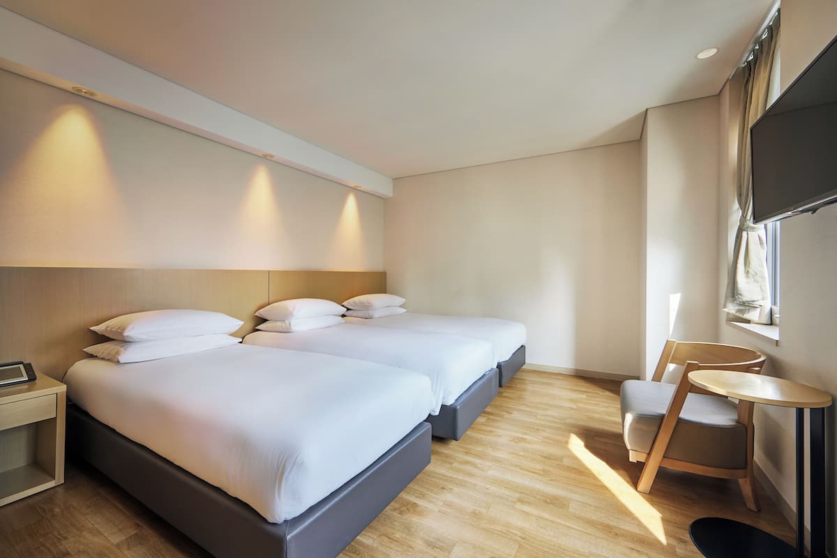 A hotel room with two beds, a small table, a chair, and a TV mounted on the wall.