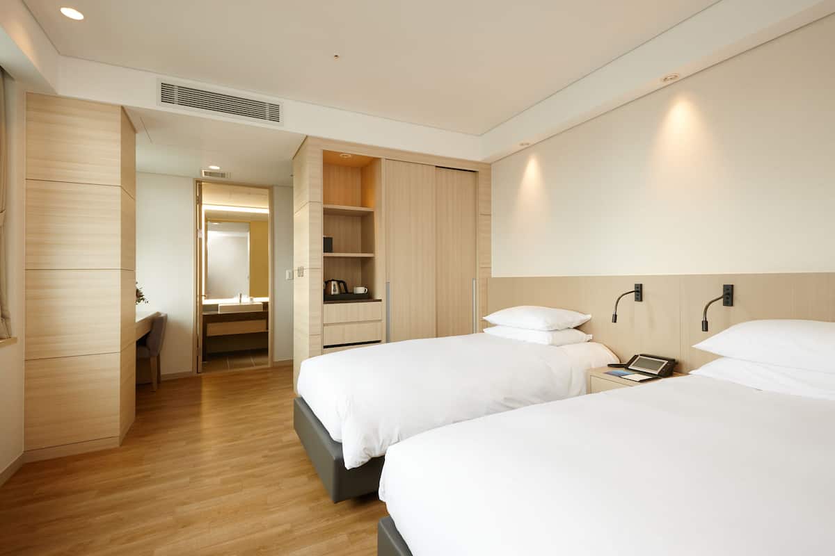 A modern hotel room with two beds, a desk, and a walk-in closet.