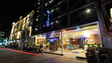 A hotel with a glass facade, outdoor seating area, and a sign indicating 'OPEN SEP 22'.