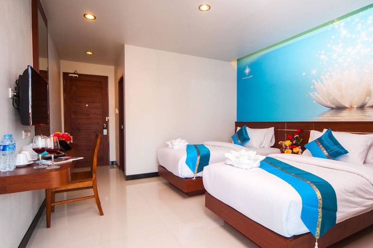 A hotel room with two beds, a desk with a chair, a television, and a large wall mural.