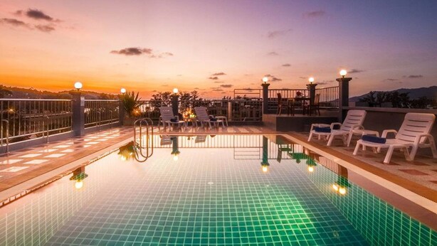 A rooftop pool with clear blue water, surrounded by lounge chairs and a railing. - The Crystal Beach Hotel (Patong)