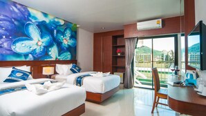 A hotel room with two beds, a desk, a large window with a view of a mountain, and a painting of flowers on the wall. - The Crystal Beach Hotel (Patong)