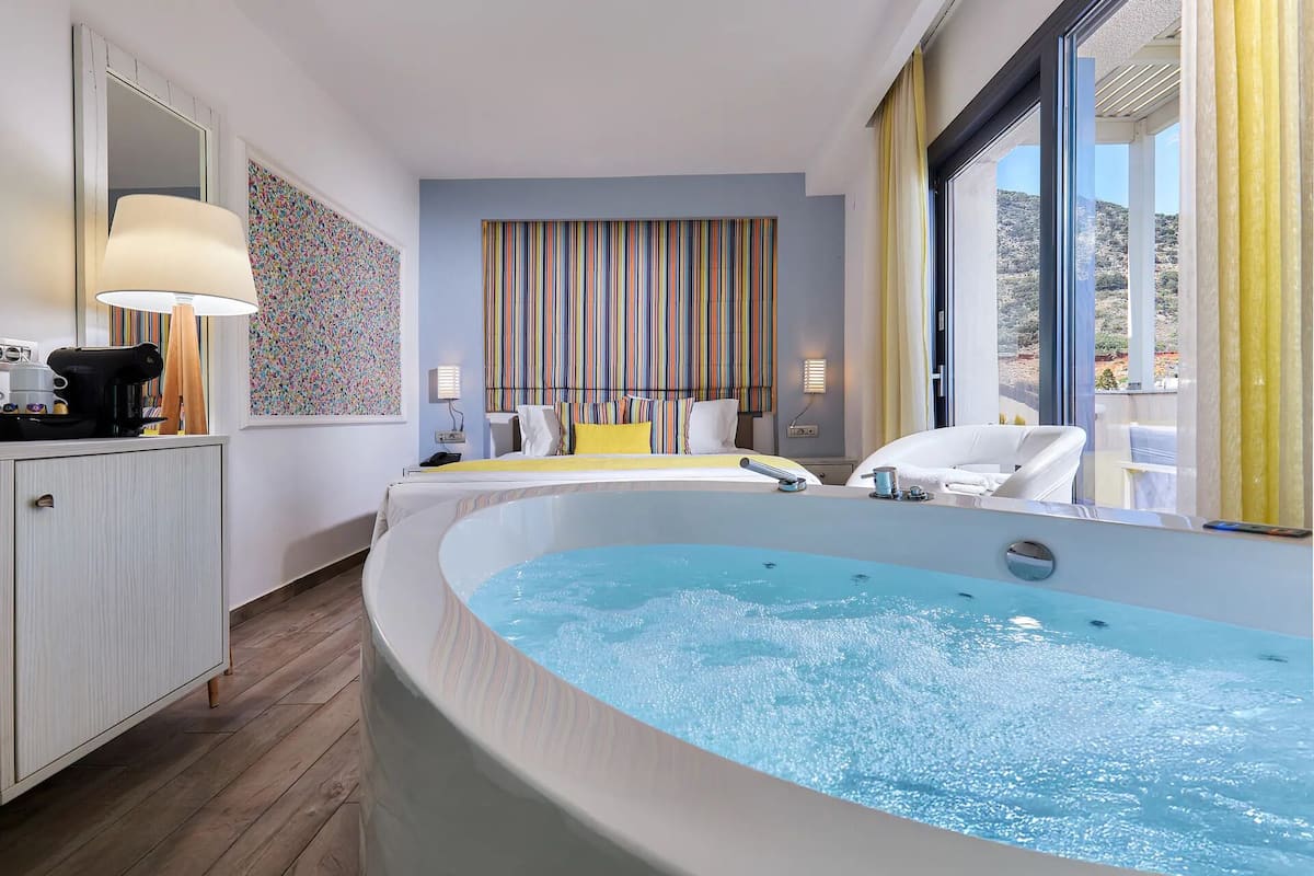 A modern bathroom with a large bathtub, a mirror, a coffee machine, and a striped wall.