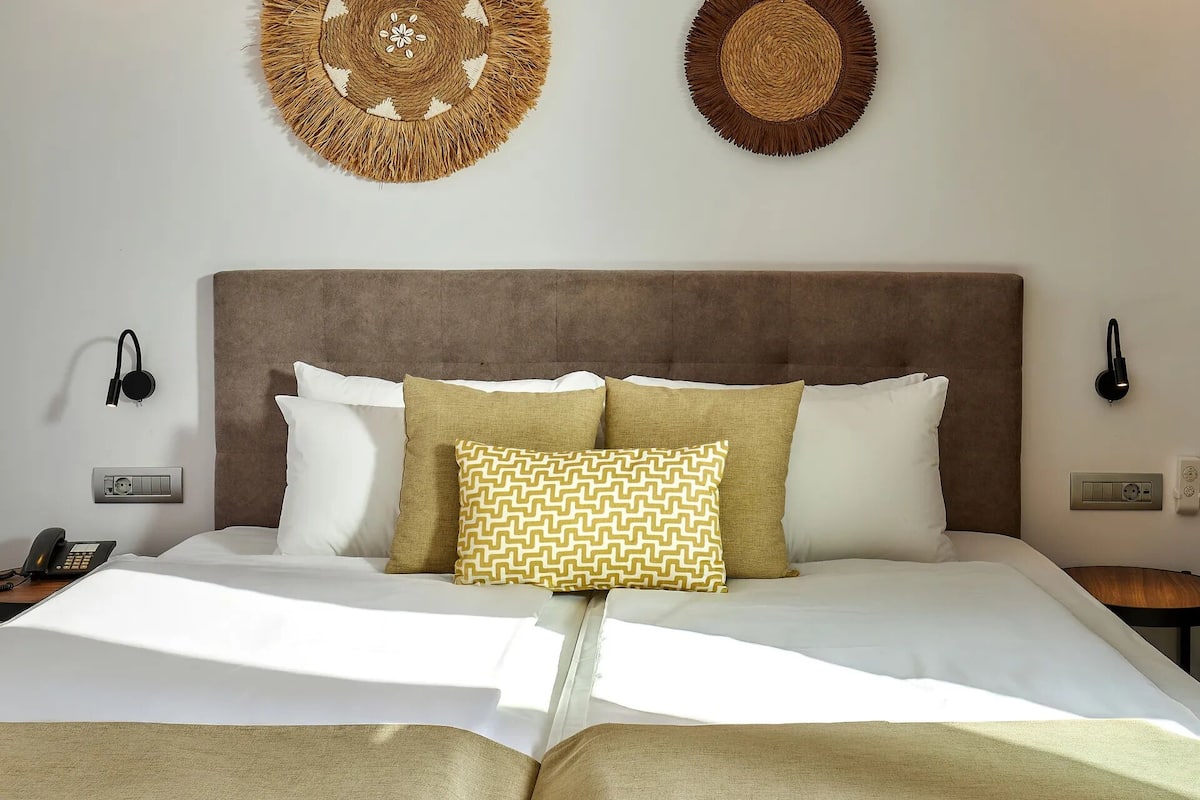 A neatly made bed with a brown headboard, white and patterned pillows, and two wall-mounted lamps.