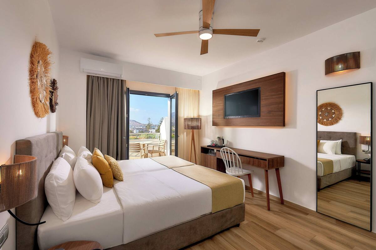 A hotel room with a bed, desk, chair, TV, and a large mirror.