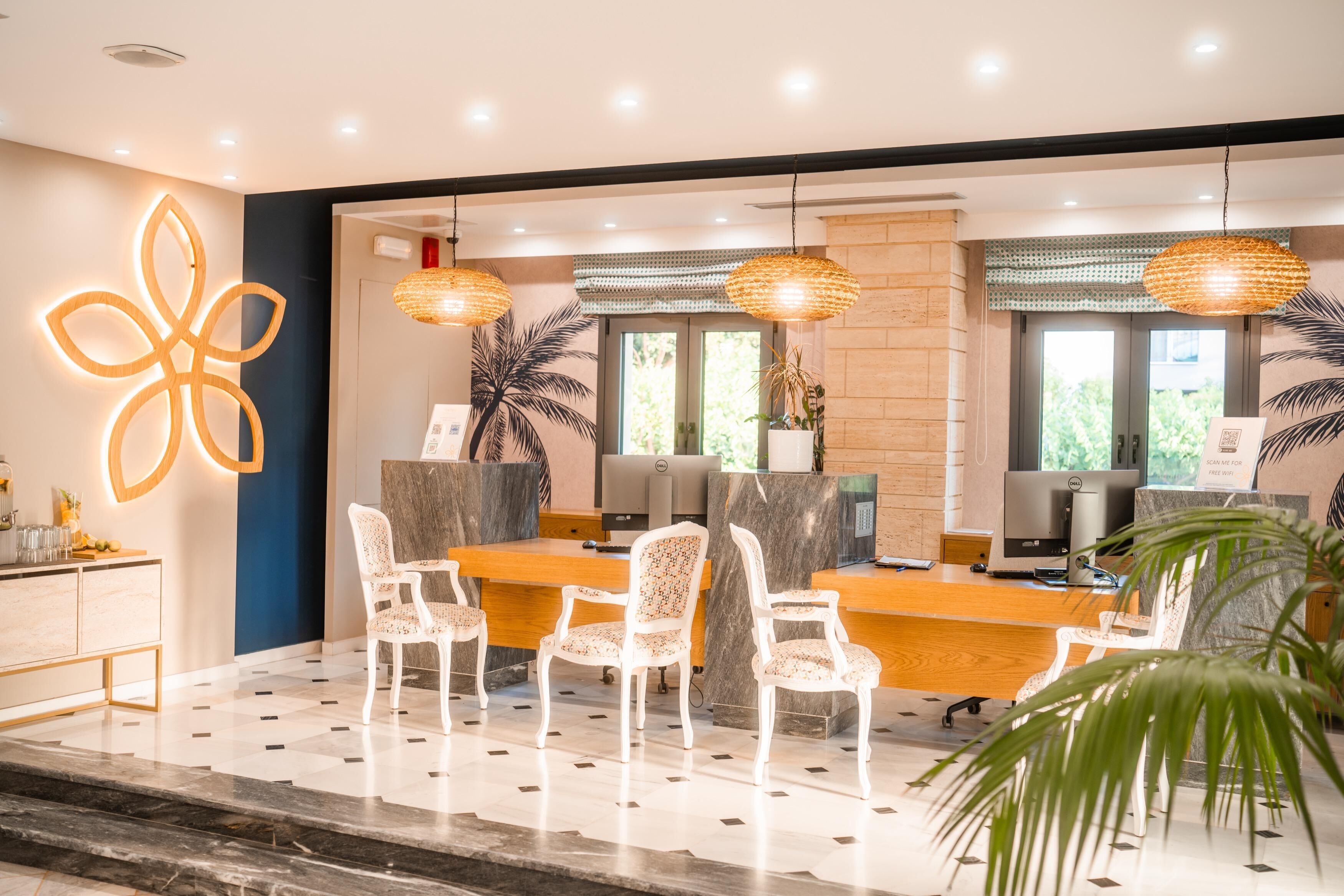 Uma área de recepção moderna, com balcão de mármore, cadeiras estofadas em branco e iluminação pendente.