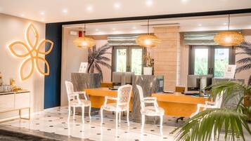 Uma área de recepção moderna, com balcão de mármore, cadeiras estofadas em branco e iluminação pendente.