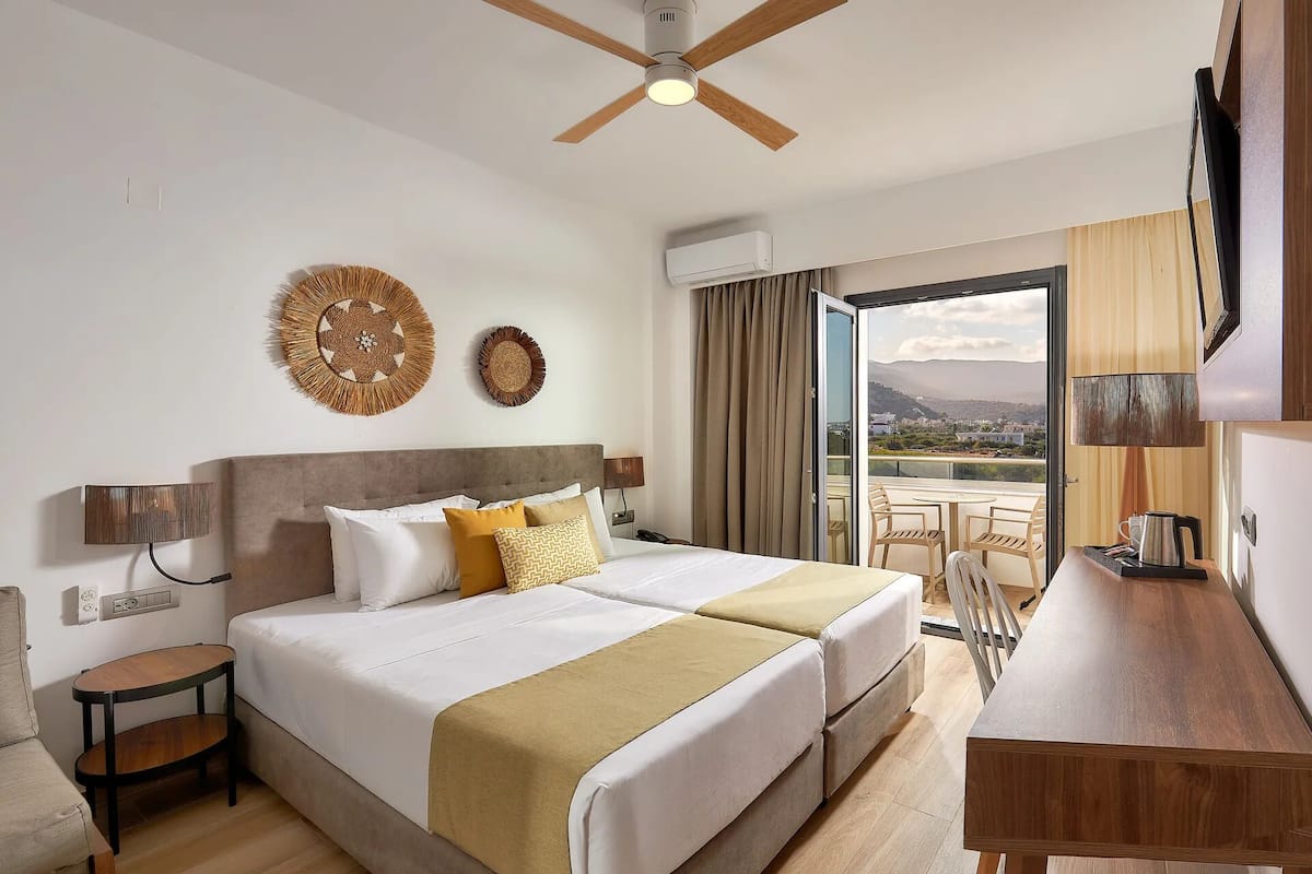 A hotel room with a bed, bedside tables, a desk, a TV, and a balcony with a view.
